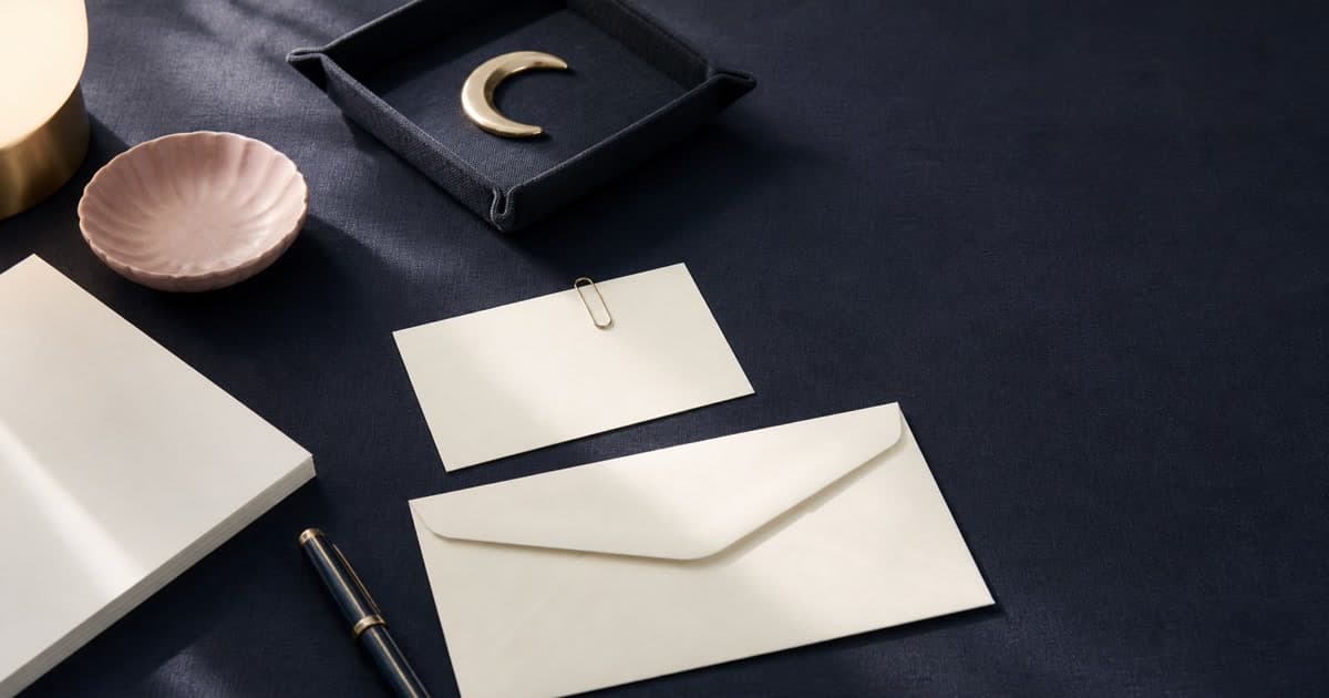 A cream bill envelope beside a small blank calendar, indigo catchall tray, gold paper clip, blush dish, and capped pen arranged for a calm repair check-in.